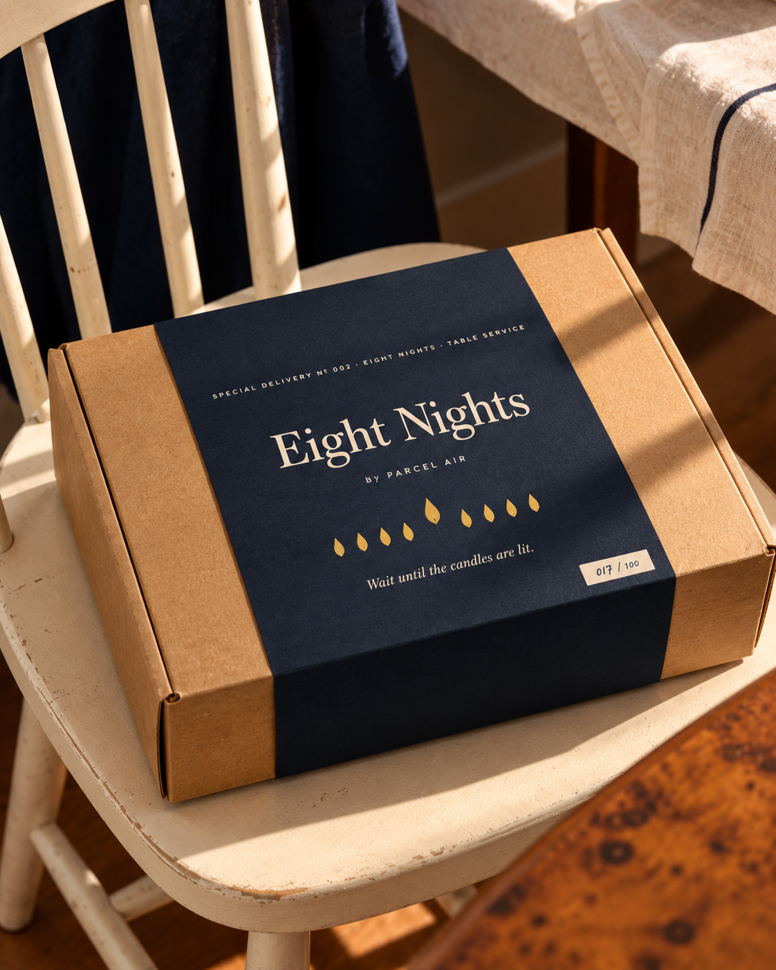 Eight Nights by Parcel Air: the kraft box with its navy Table Service sleeve, on a kitchen chair
