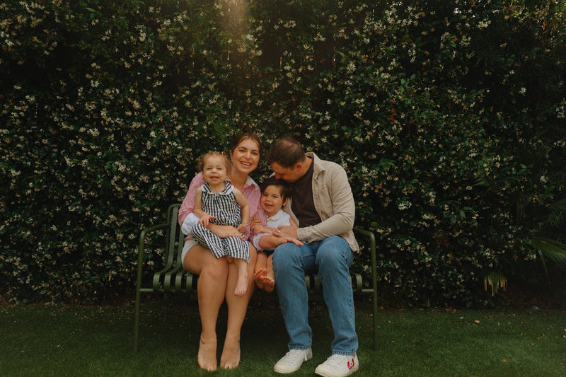 Elizabeth, founder, and her family of four sitting on a bench in front of a green hedge